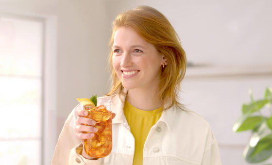 "Een persoon die geniet van een verfrissend glas ijsthee, met condensatie op het glas dat de koude inhoud aangeeft. Ze houden het glas voorzichtig vast terwijl ze aan het rietje nippen, de zichtbare vreugde en ontspanning op hun gezicht onderstrepend het zomerse gevoel.