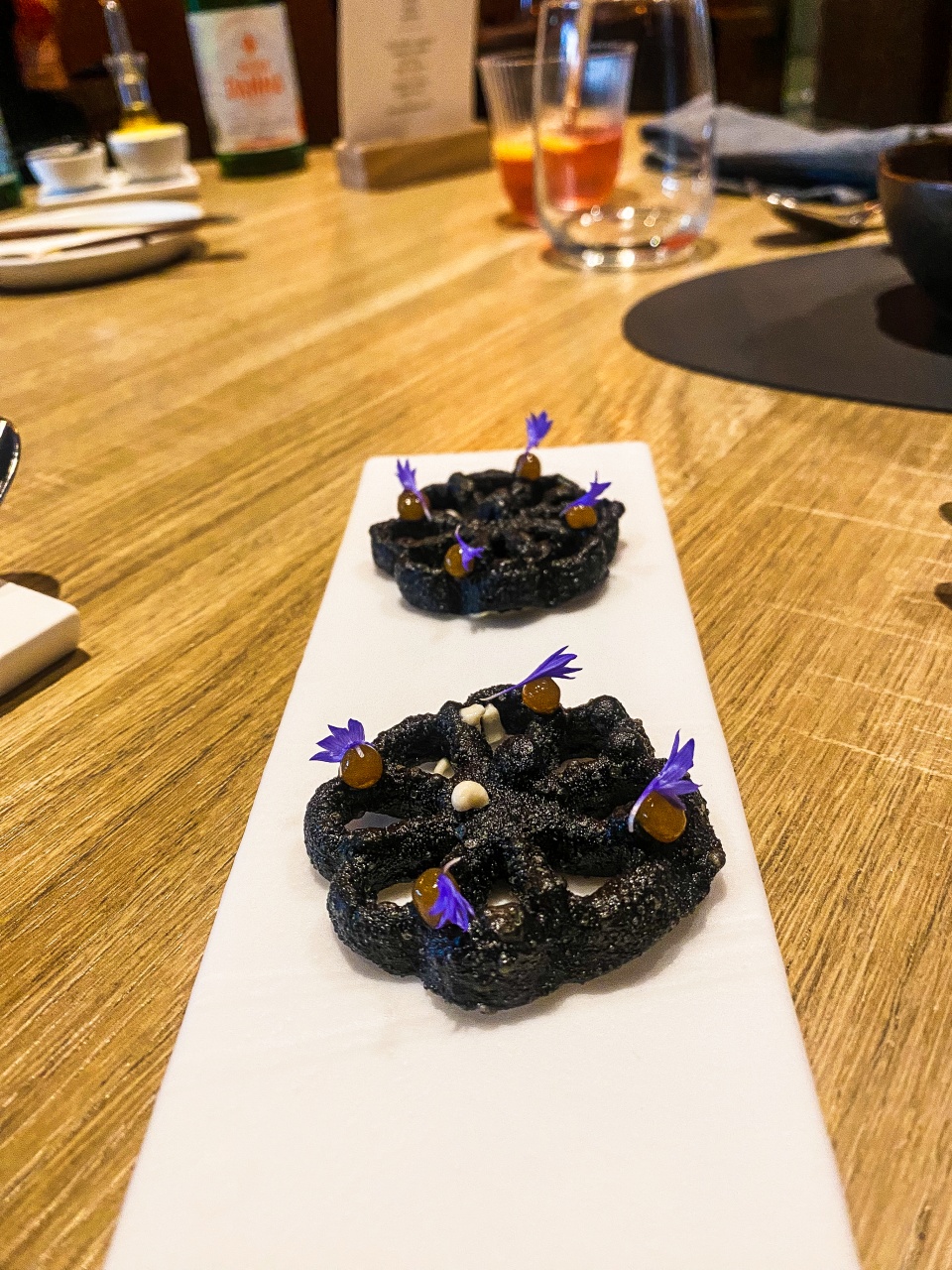 Een knapperige buñuelo, rijkelijk gevuld met gerookte oosterschelde paling en kombu, gepresenteerd op een verfijnd bord, weerspiegelt de culinaire creativiteit van Restaurant Zappaz in Leuven