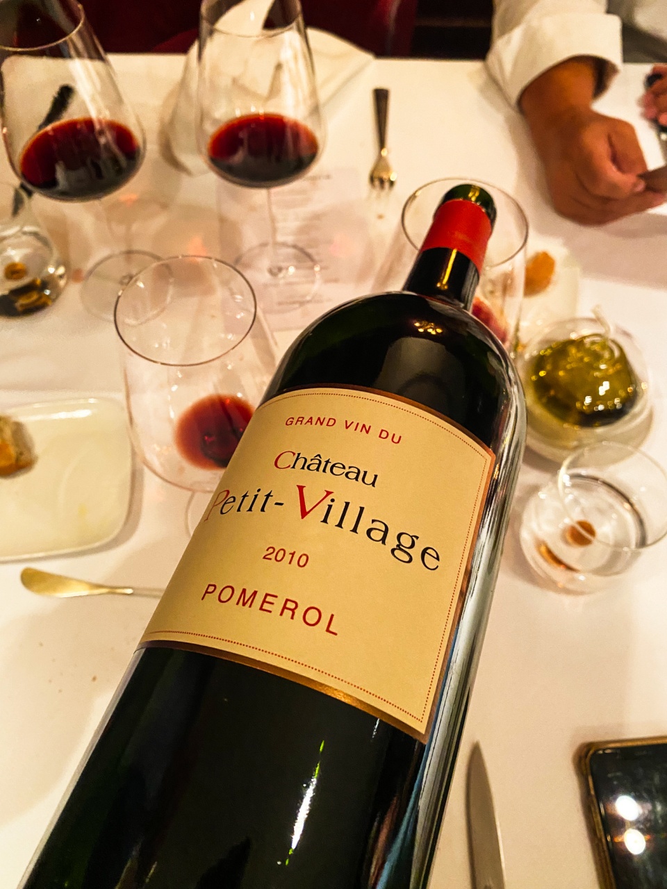 Bottle of wine from Château Petit Village, millésime 2010, elegantly poured into a glass