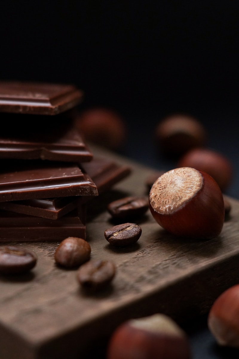 Finely detailed close-up of glossy dark chocolate pieces stacked on a rustic wooden base, with melted chocolate drops suggesting the rich texture and flavor.