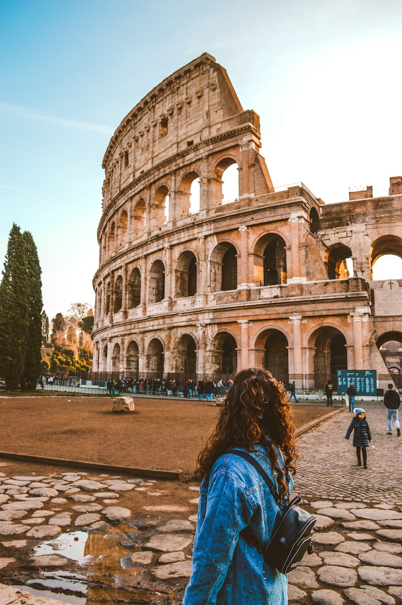 Tourists admire the majestic Colosseum in Rome, with the ancient amphitheater prominently displayed against a bright autumn sky.
