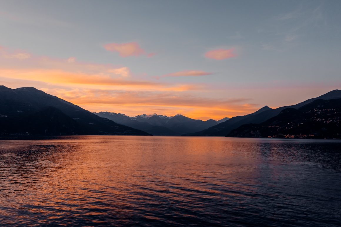 Serene image of Lake Como, with crystal clear water reflecting the surrounding mountains and picturesque villages on the shore, while a few small boats glide gently across the surface.