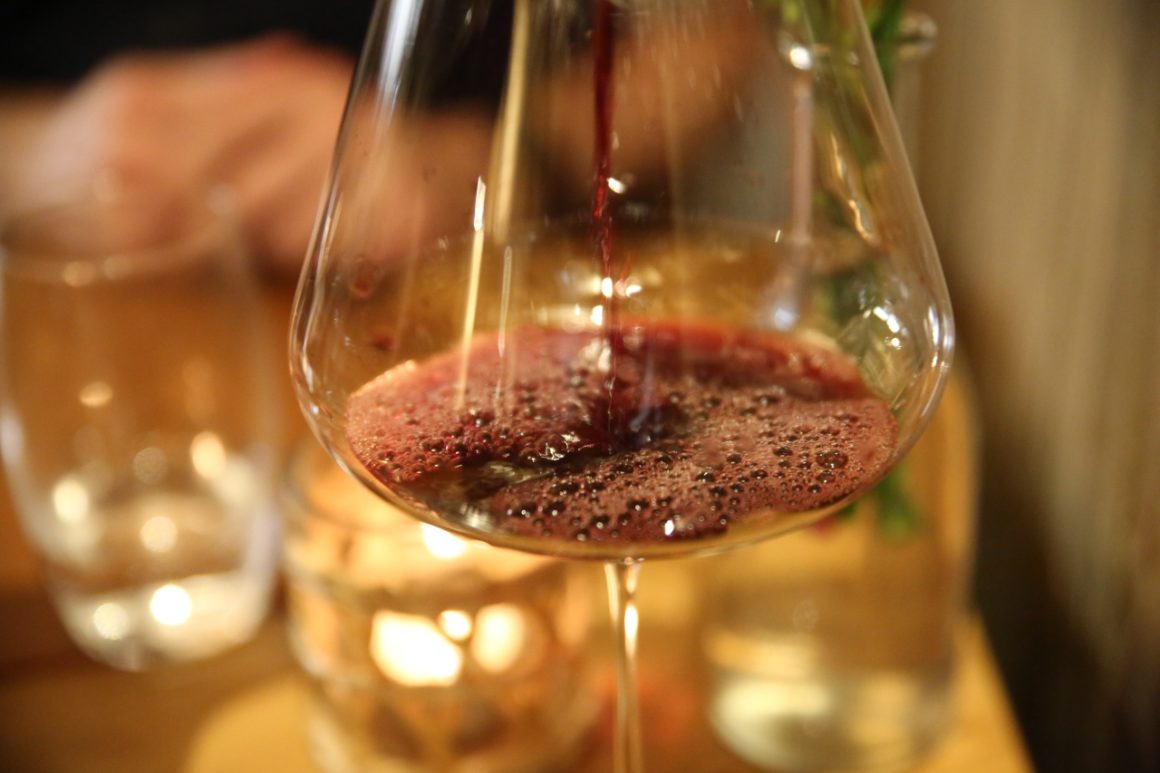 Een elegant glas wijn, gevuld tot de perfecte hoogte. Het rijke kleurenpalet van de wijn, mogelijk een rode of witte variant, glinstert subtiel bij het vangen van het licht. De helderheid van de wijn en de manier waarop hij in het glas rust, suggereren een wijn van hoge kwaliteit. 