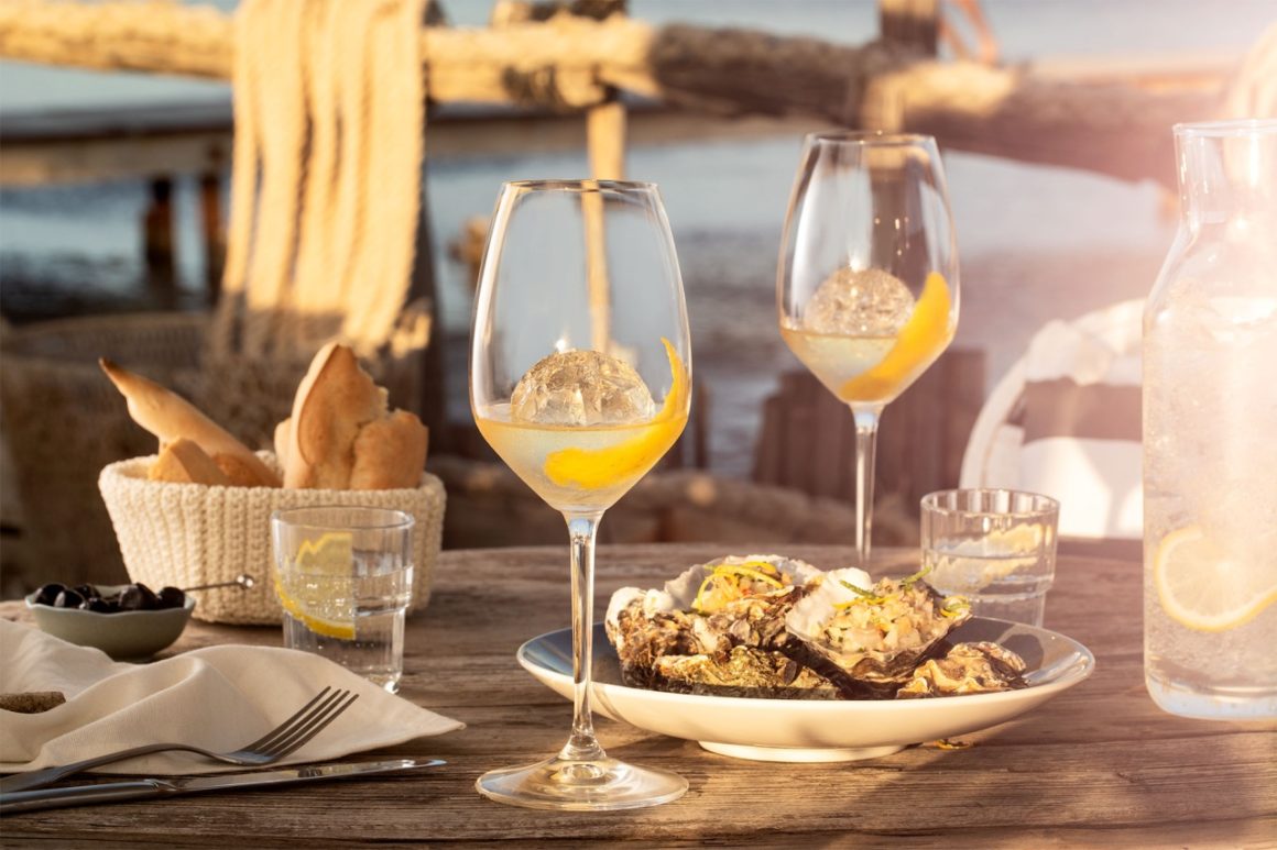 Verse oesters op een bedje van ijs naast een heldere cocktail, symboliserend de harmonieuze combinatie van zilte smaken en de verfijning van Noilly Prat vermout.