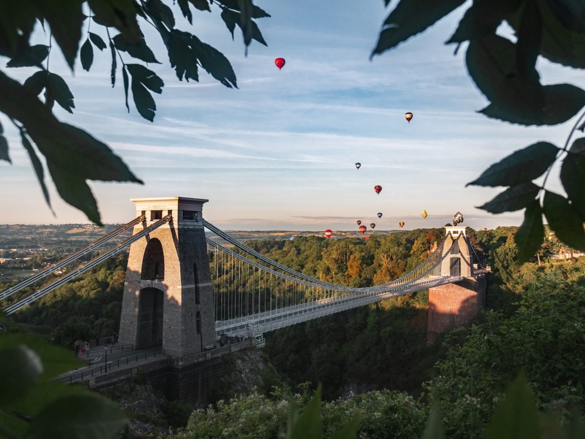 FOTO VAN DE INDRUKWEKKENDE SUSPENSION BRIDGE MET KABELS EN TORENS, OVERSPANNEND OVER EEN RIVIER MET EEN WEIDS UITZICHT OP DE OMGEVING