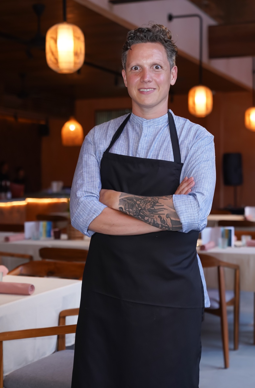Chef-kok Syrco Bakker poseert met een zelfverzekerde glimlach in de eetzaal van zijn restaurant