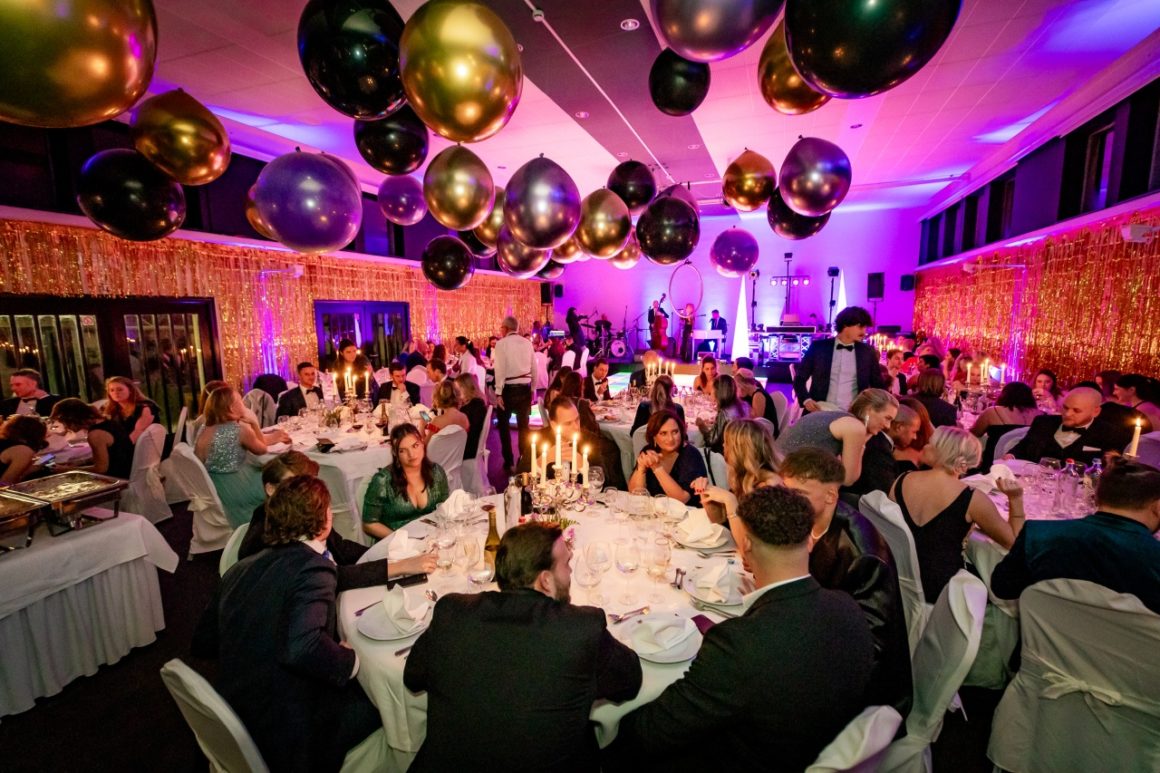 Overzicht van een feestzaal met gasten die dineren, met een focus op de tafels en ballonnen decor.
