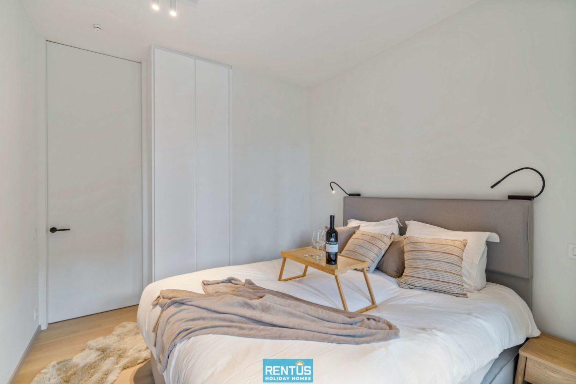 Slaapkamer met dubbel bed, minimalistische inrichting en een dienblad met wijn op het bed.