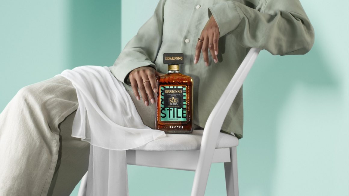 Disaronno Stile limited edition fles op de schoot van een vrouw in een minimalistische, mintgroene outfit, zittend op een witte stoel met een witte sjaal.

